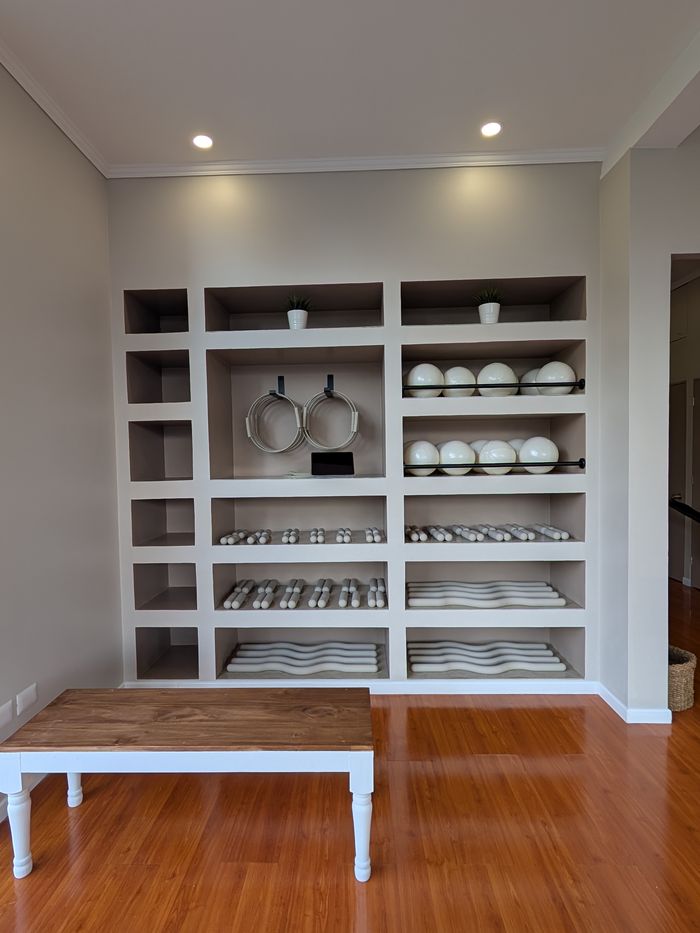 Estantería del estudio con pelotas, aros de pilates, mancuernas y colchonetas ordenadas